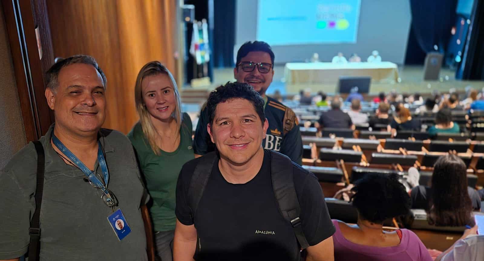 inserir aqui Quatro profissionais sorrindo em mesa de reunião, com esqueleto humano e de felino ao fundo, representando parceria CSM Minas e Museu da PUC.