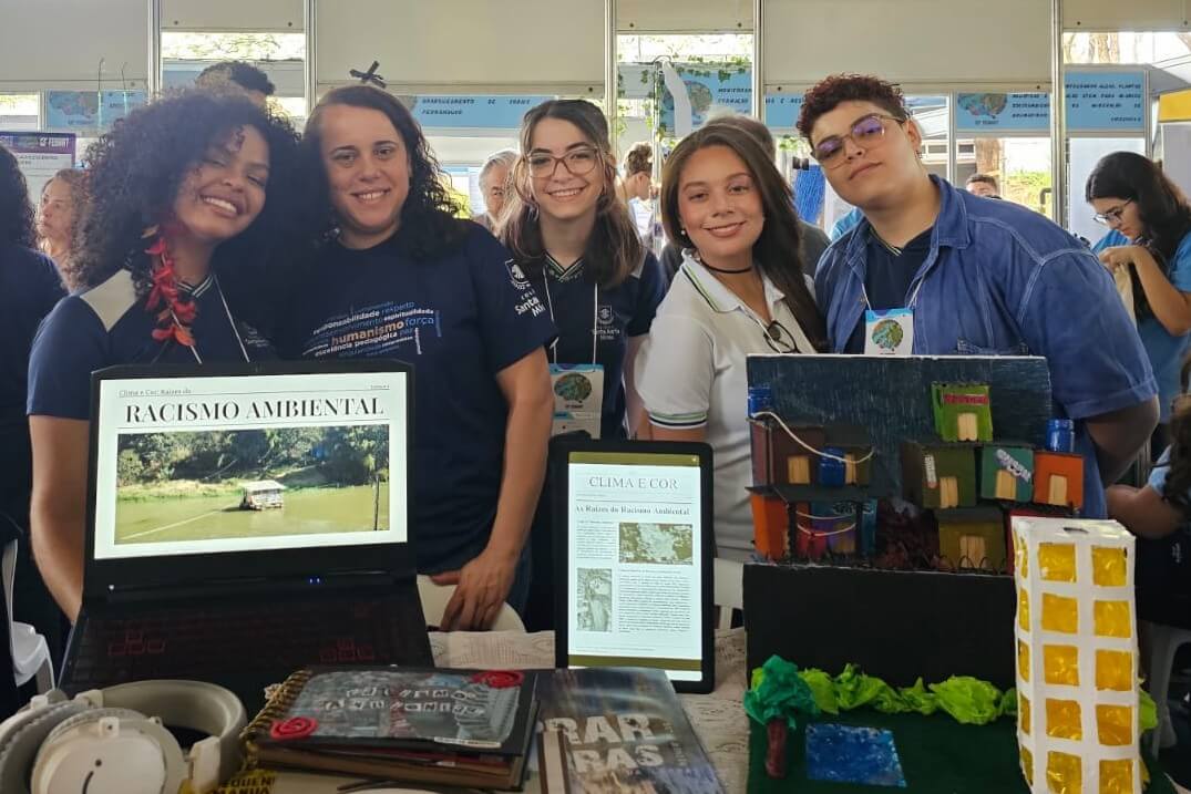 inserir aqui Estudantes do CSM Minas, convidados para a Genyus Olympiad, apresentam projeto sobre racismo ambiental com laptop e maquete.